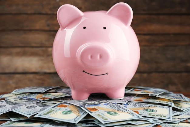 Pig money box and dollar banknotes on wooden wall background