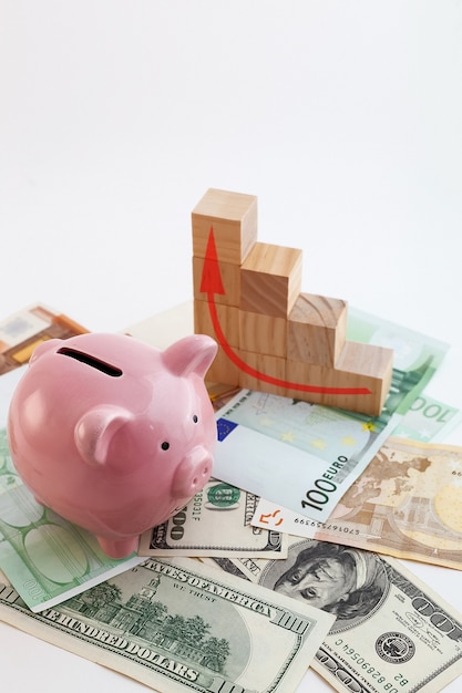 Pig shaped piggy bank, growing graph wood cubes, euro banknotes and us dollars on isolated white background