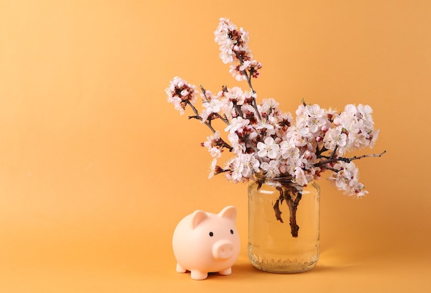 Piggy bank and Beautiful flowering branches in glass jar on orange background