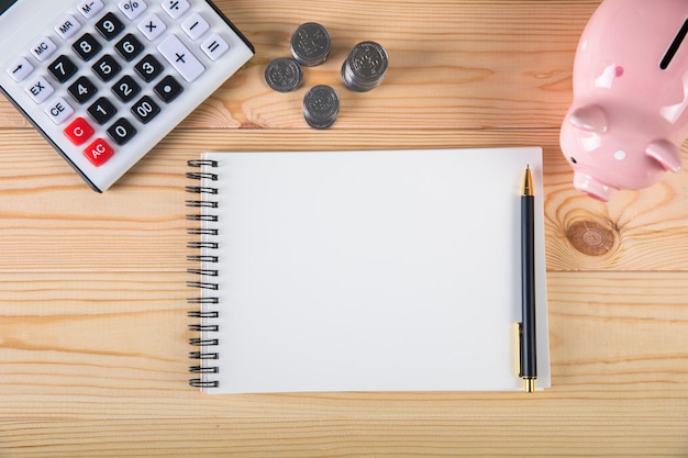 Piggy bank, calculator and coins on wooden surface