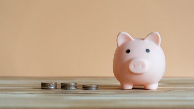 Piggy bank and coins stacks placed on a wooden table with light orange background