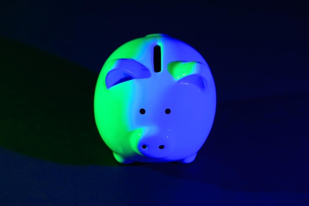 Piggy bank on a dark background with greenblue backlight Banking concept Bright neon lights on a black background