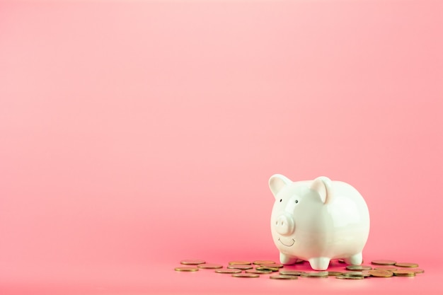 Piggy bank and a golden coins pile on pink background. 