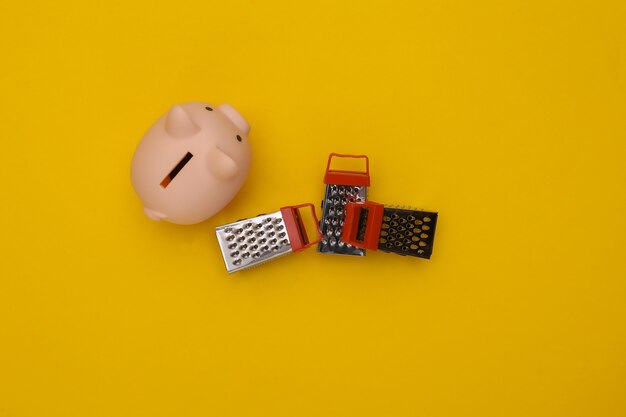 Piggy bank and mini graters on yellow background. Top view