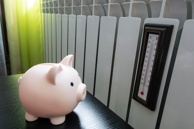 Piggy bank and thermometer on radiator Saving heating in winter Energy crisis energy efficiency and rising heating costs in Europe