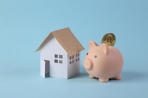 Piggy bank with bitcoin and model house on blue background Savings concept