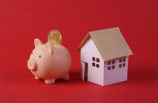 Piggy bank with bitcoin and model house on red background Savings concept