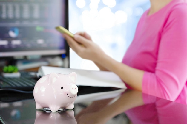 Piggy bank with blur woman holding mobile phone and stock chart in computer monitor background Online business concept