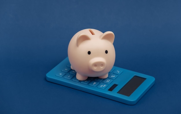 Piggy bank with calculator on classic blue background