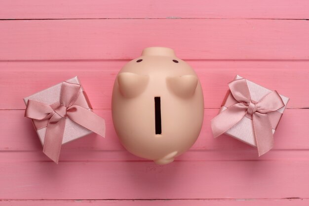 Piggy bank with gift boxes on pink wooden surface. Top view