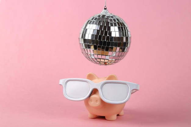 Piggy bank with glasses under disco ball on pink background Minimalism party concept