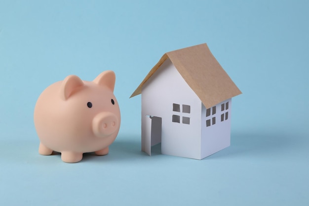 Piggy bank with small model house on blue background Savings concept