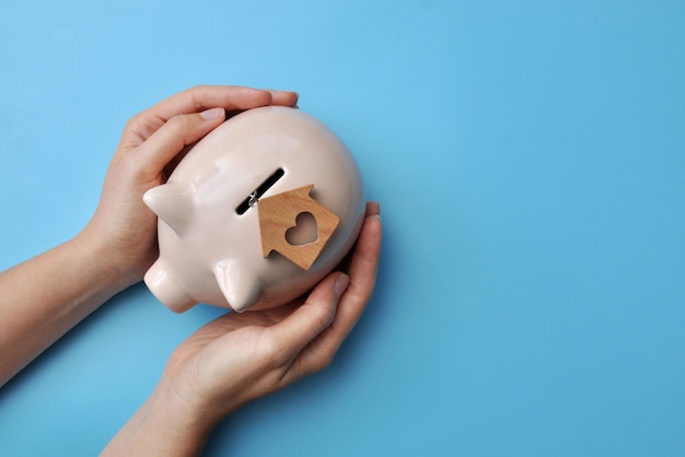 A piggy bank and a wooden house nearby a symbol of saving money