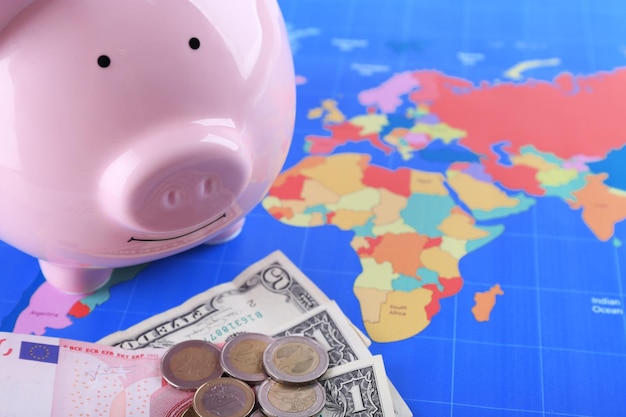 Piggy money box banknotes and coins on world map background closeup