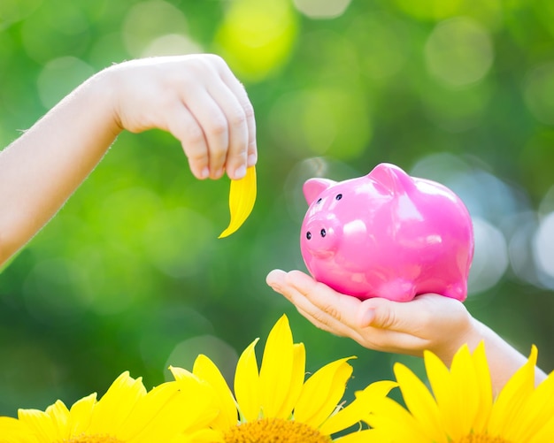 Piggybank and leaf in hands against green spring background Shallow depth of field