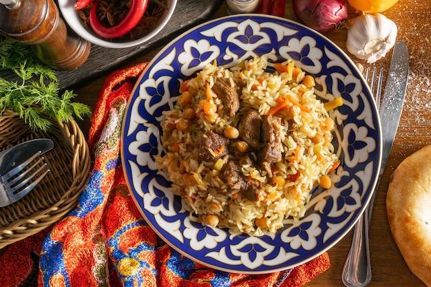 Pilaf with lamb. Traditional oriental hot dish of rice, lamb and yellow carrots with garlic, raisins, chickpeas and turmeric in a plate with a national Uzbek ornament.