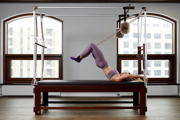 Photo pilates aerobics instructor woman in fitness exercise on cadillac reformer musculoskeletal system training on modern reformer simulator