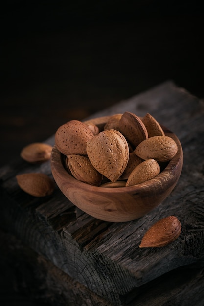 Pile of Almond nuts in a bowl on a dark wooden surface. Fresh nuts in their shells.