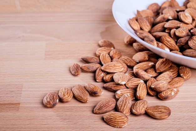 Pile of almonds in white dish on wooden floor.