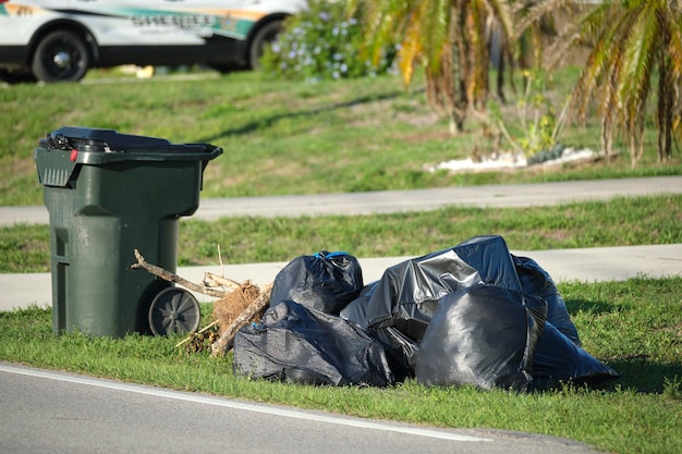 Pile of black garbage bags and plastic dustbin outdoors on rural street side Waste management problems