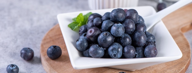 Pile of blueberry fruit in a bowl plate on a tray over gray cement concrete background, close up, healthy eating design concept.