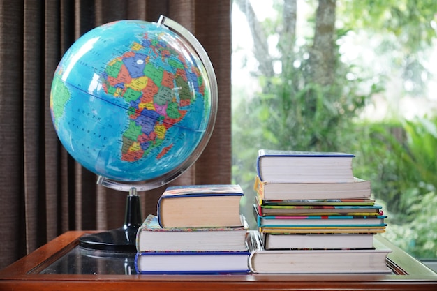 Pile of books and mock earth globe on table in brown curtain background