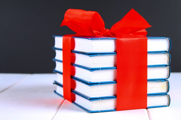 A pile of books tied with a red ribbon on a white wooden table. gift on background of a chalkboard