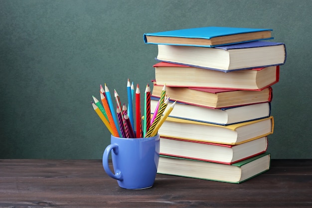 Pile of books with color covers and colored pencils in a cup on a wooden table