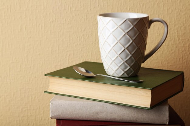 Pile of books with cup and spoon on light wall background