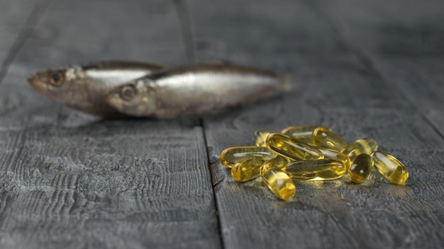 A pile of capsules with fish oil on the background of two fish on a wooden table