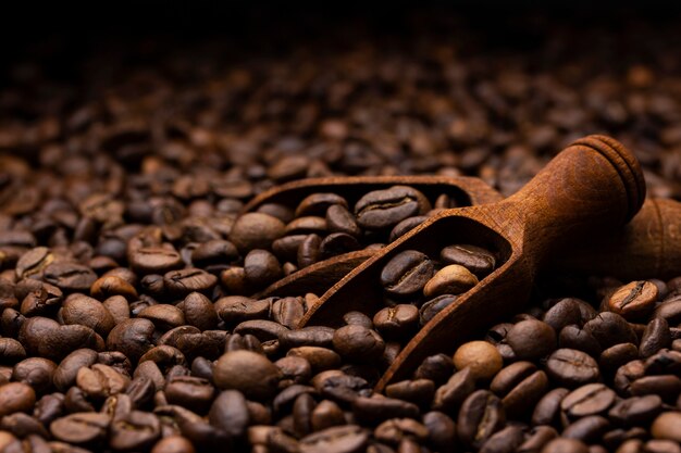 Pile of coffee beans with wooden scoop, close up, dark background with copy space