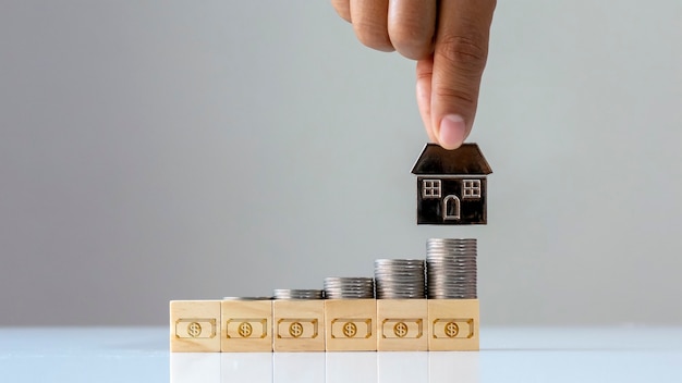 A pile of coins on a wooden block with money icon and a house mobile finance and investment concept about real estate company.