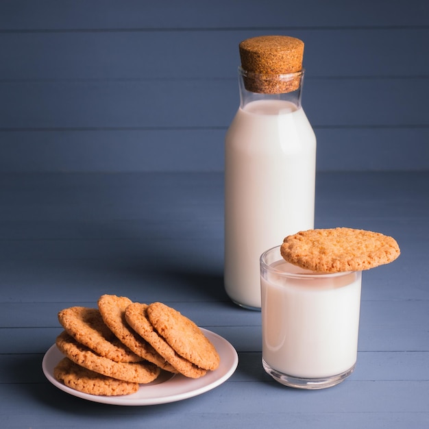 A pile of delicious homemade cookies on a white plate a bottle of milk and a glass of milk on a blue wooden background