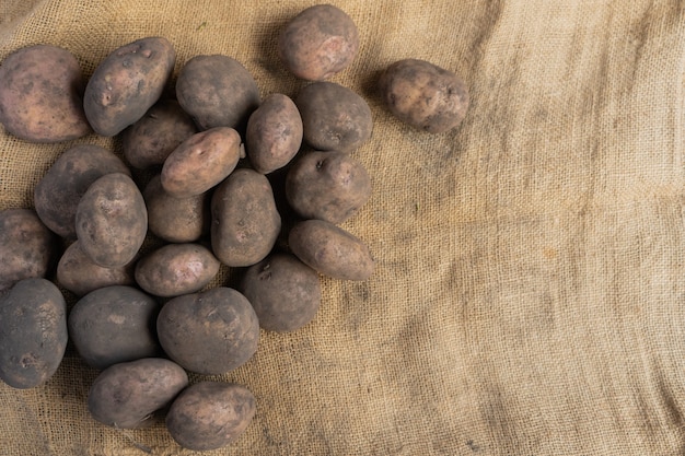 Pile of dirty potatoes on the left side of a jute mat