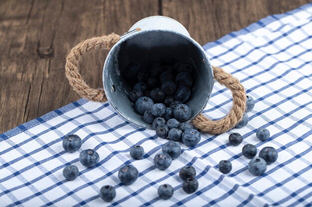 Pile of fresh blueberries out of metal bucket on wooden background. 