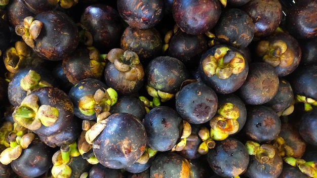 Photo pile of fresh mangosteens at a market stall displaying dark purple fruits with green caps in a vibrant and detailed close up