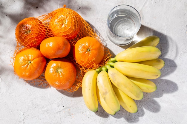 Pile of fresh tangerines bananas and glass with water on the concrete table