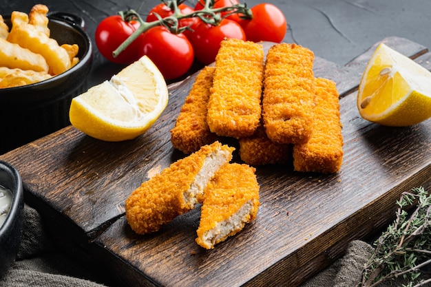 Pile of golden fried fish fingers with white garlic sauce set, on wooden cutting board, on black background