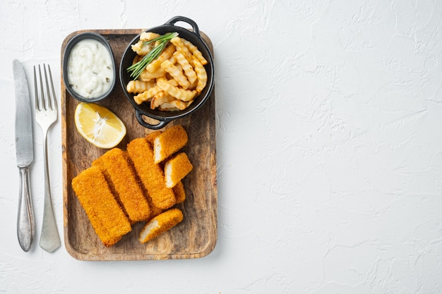 Pile of golden fried fish fingers with white garlic sauce set on wooden tray