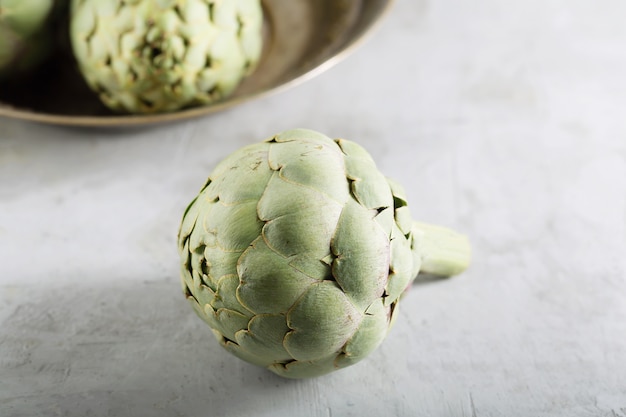 Pile of green Spanish or Italian Artichokes on the metal rustic plate and gray table, close up