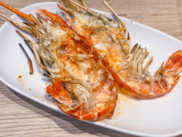 Pile of Grilled giant river prawn shells on white dish on wooden table as background. Popular Thai food