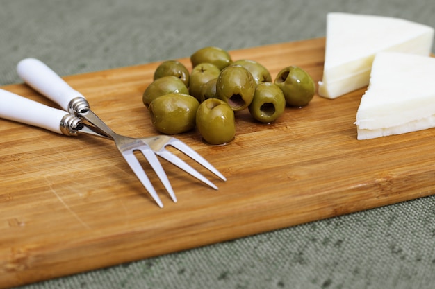 Pile of Italian green olives and goat cheese on wooden desk on fabric tablecloth.