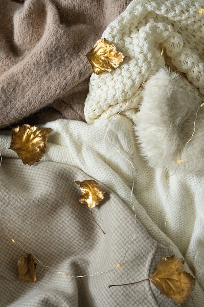 Pile of knitted clothes with autumn gold leaves warm background knitwear space for text autumn winte...