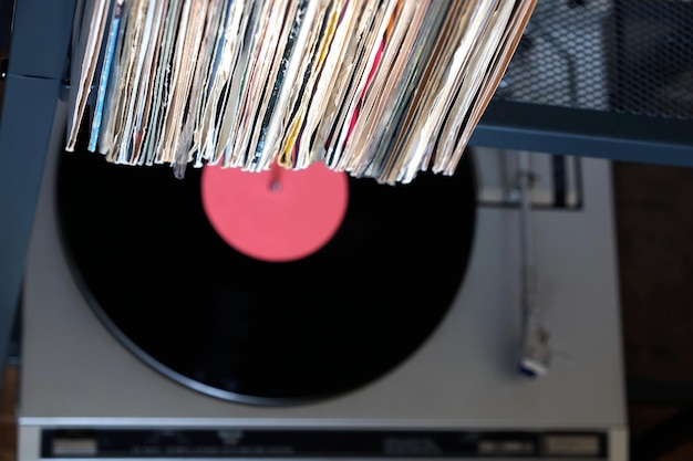 Pile of many close standing vinyl records in old covers and turntable in gray case on a desk