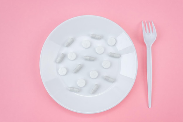 A pile of medical pills with a fork on a plate on a pink background. Pill overdose concept.