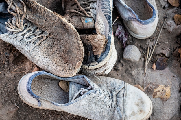 A pile of old dirty shoes lies on the ground. Worn out shoes. Poverty and misery concept.