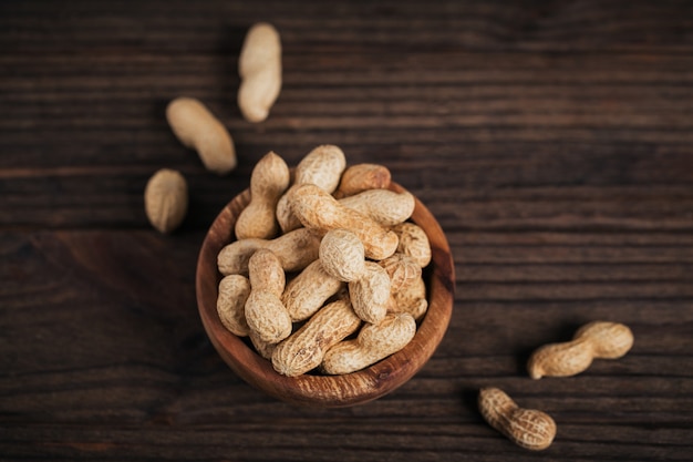 Pile of Peanuts in a bowl on a dark wooden background. Fresh nuts in their shells.