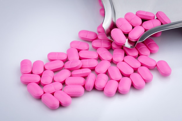 Pile of pink tablets pill on white background near stainless steel drug tray.