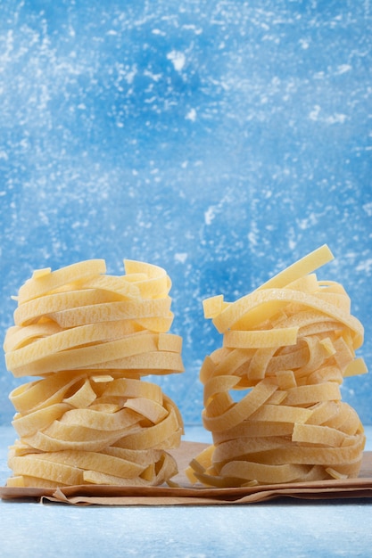 Pile of raw Italian tagliatelle noodles isolated on blue background.