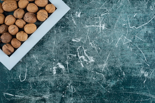 Pile of shelled walnuts with empty frame on marble table.